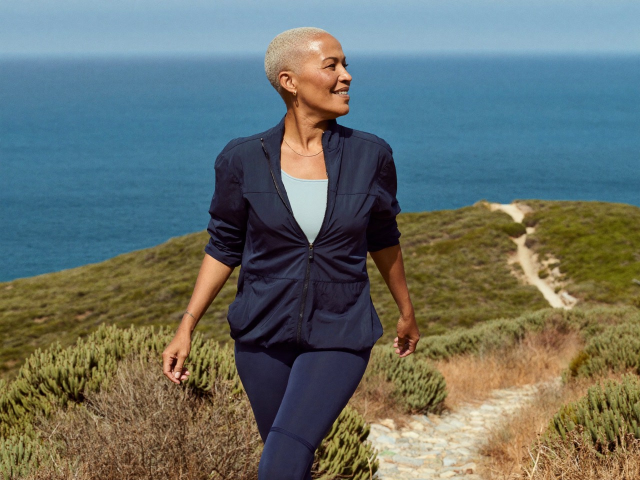 A woman in her sixties walking a coastal trail high above the ocean