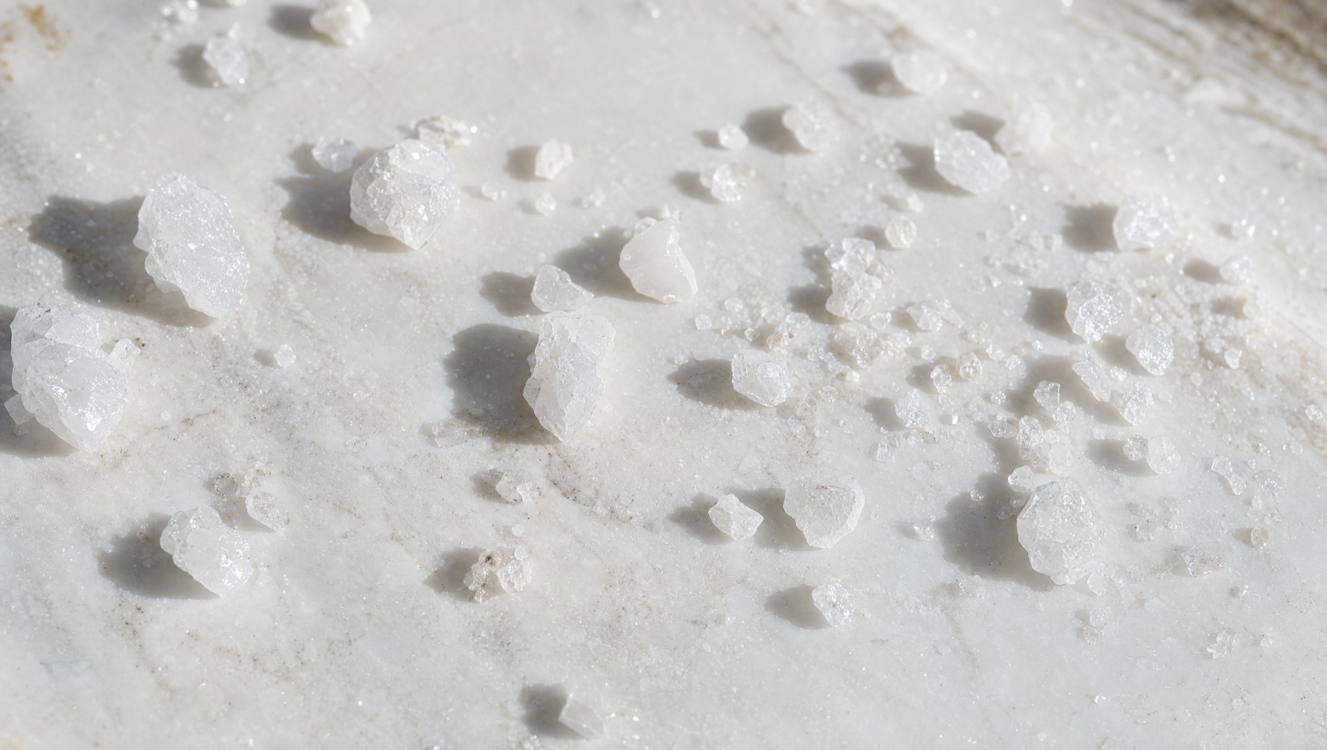 Sea salt crystals on white marble in bright sun